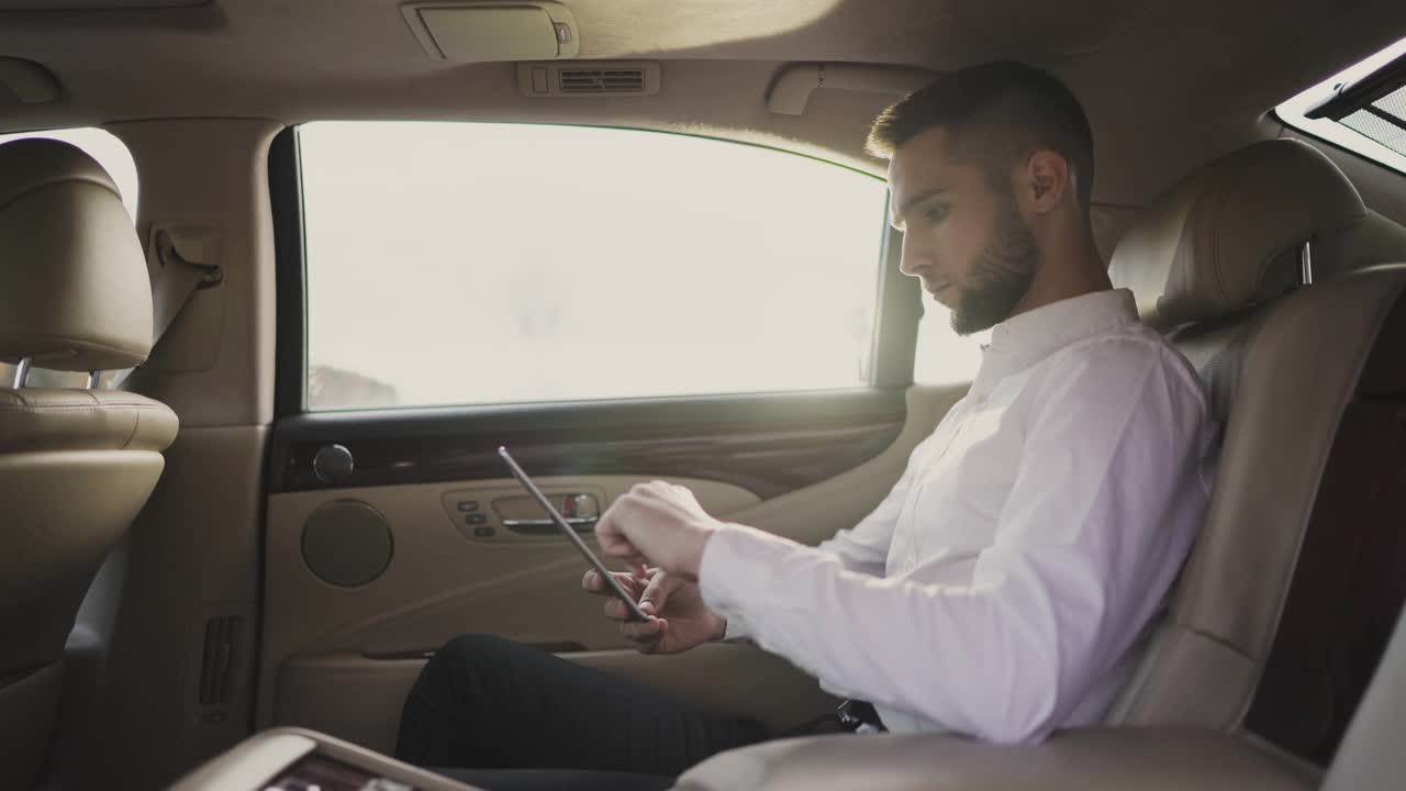 一名男子坐在汽车后座上使用平板电脑视频素材