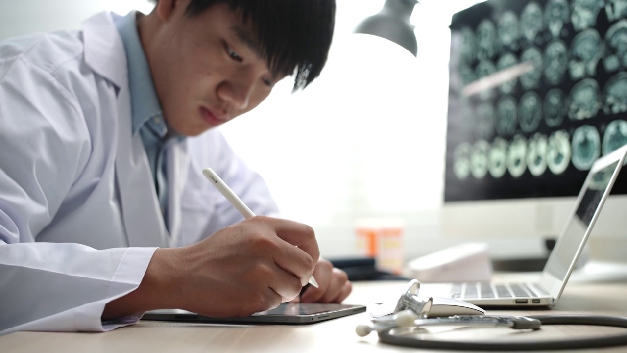 亚洲男医生在医院办公室办公桌上的数字平板电脑上工作视频素材