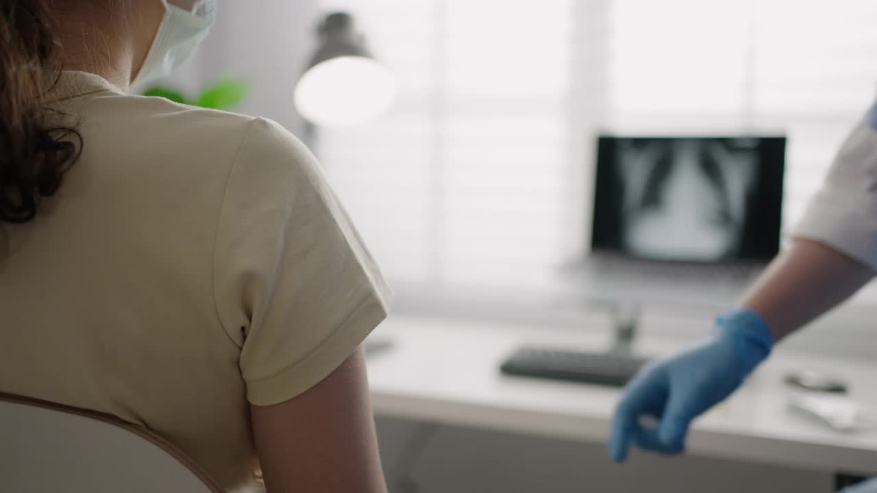 在诊所或医院办公室为佩戴口罩的患者接种Covid-19或流感病毒疫苗的女护士视频下载