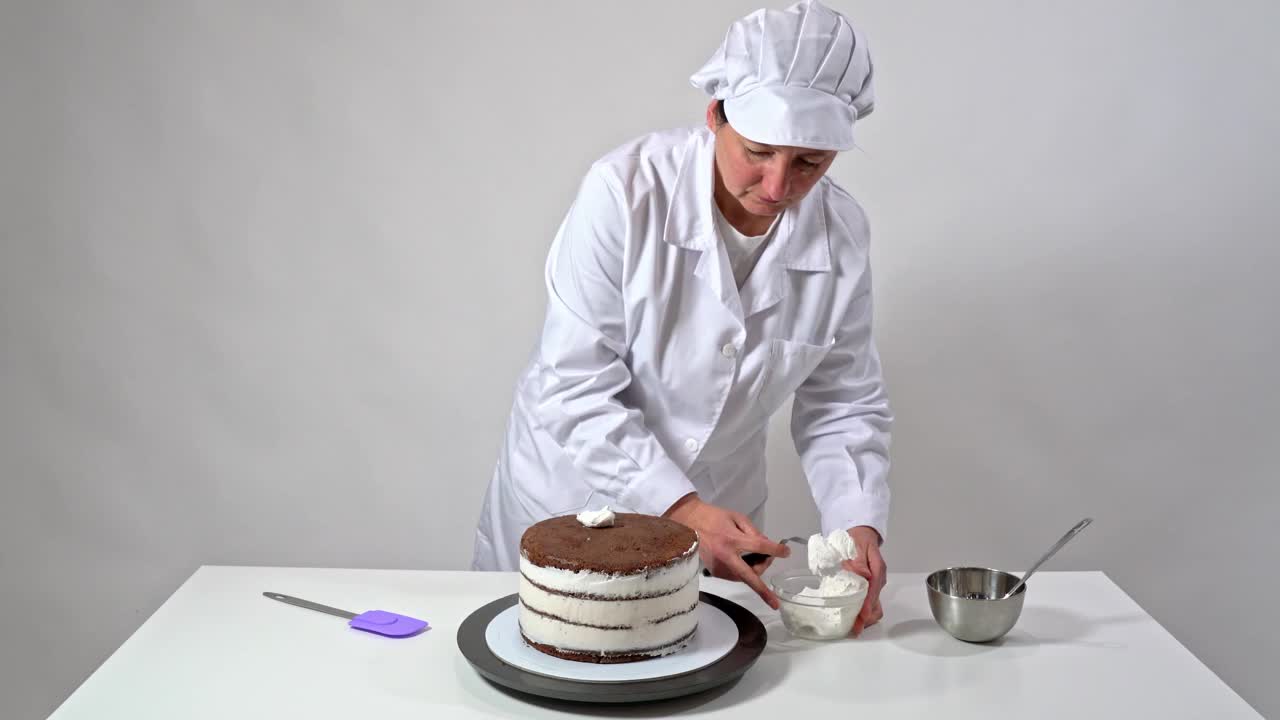 前面的镜头，一个面包师使用糖霜抹刀小心地触摸奶油覆盖蛋糕的侧面。视频下载