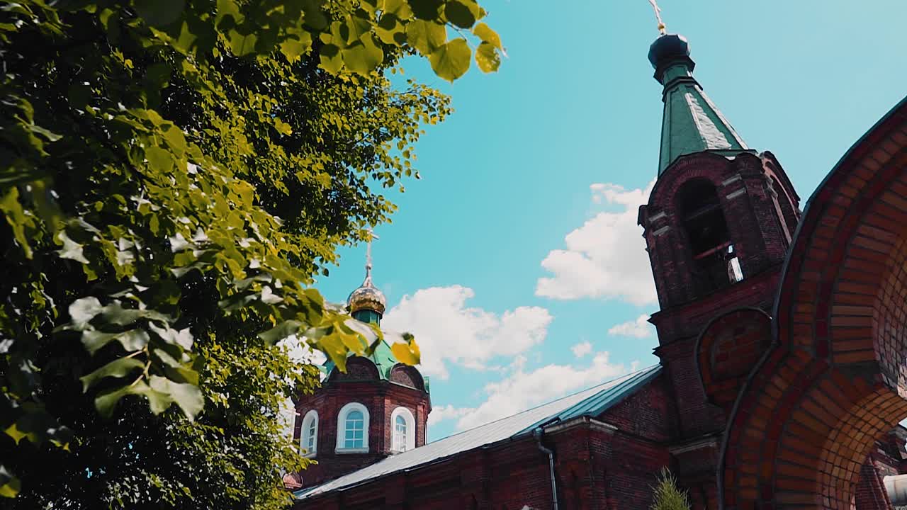 镜头捕捉到了树林中一座美丽的红砖教堂。背景是蓝色的天空和太阳。视频下载