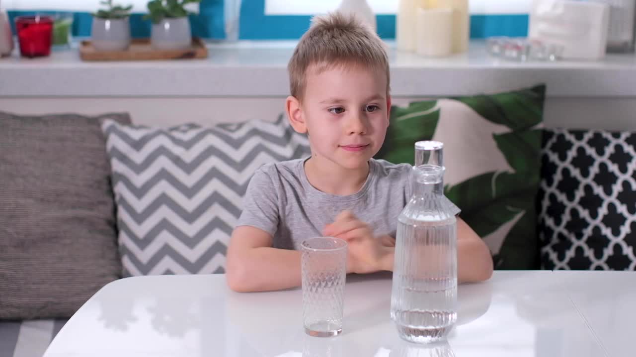 一个可爱的男孩把水瓶里的水倒进杯子里，然后喝下去。视频素材