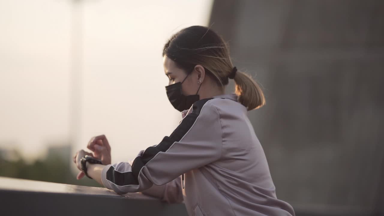 女性跑步者戴面罩，在户外使用健身追踪器视频素材