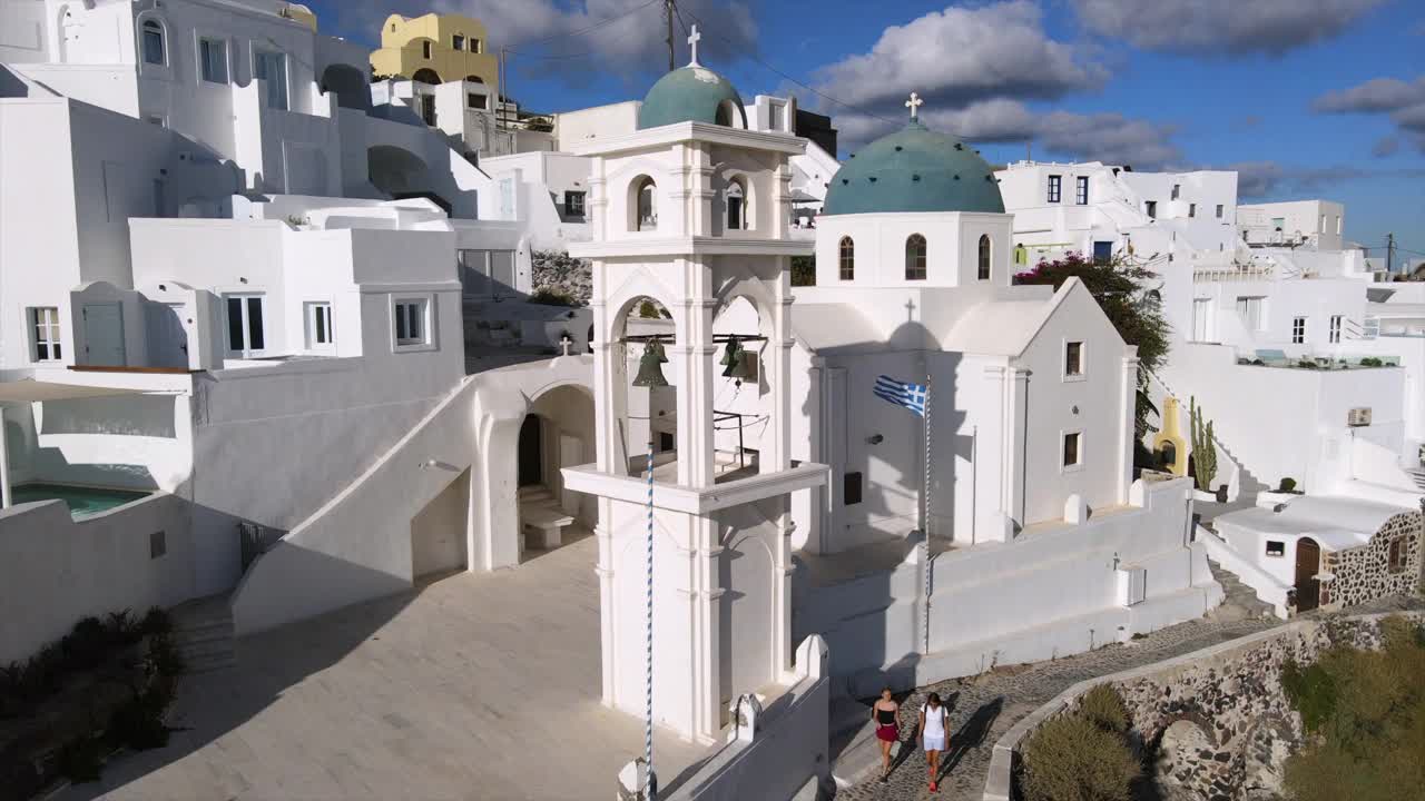 在阳光明媚的日子里，无人机在希腊圣托里尼市上空盘旋，拍摄城市里著名的阿纳斯塔西东正教教堂视频素材