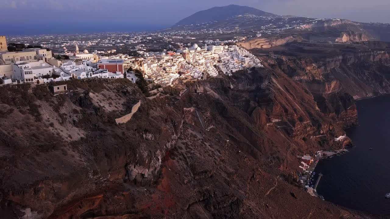 空中平移拍摄的东正教大教堂在城市，无人机飞向山上的建筑物在日落-圣托里尼，希腊视频下载