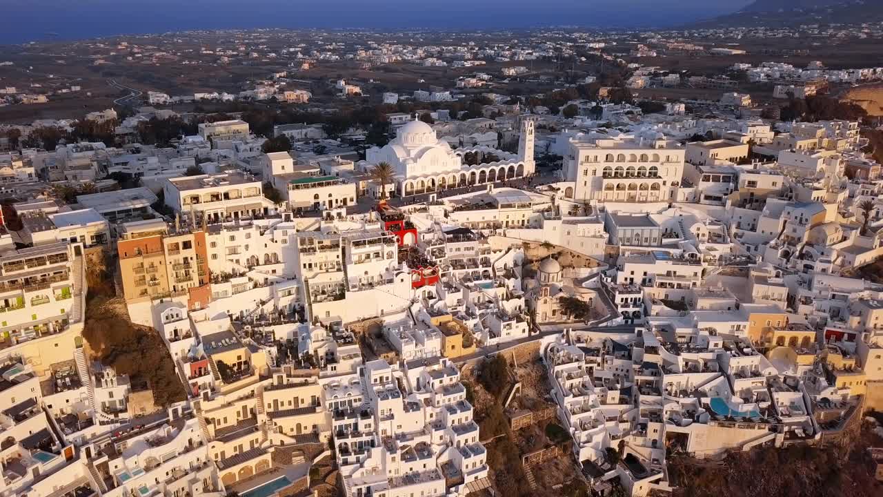 空中平移拍摄的东正教大教堂在城市，无人机向后飞从山上的建筑物在日落-圣托里尼，希腊视频素材