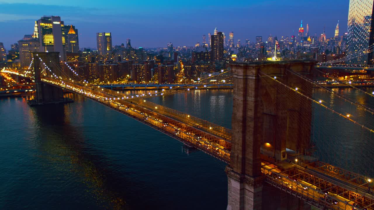 从布鲁克林大桥上鸟瞰曼哈顿的交通，以曼哈顿中城的天际线为背景，在夜晚被照亮。无人机视频与广泛的轨道摄像机运动。视频下载