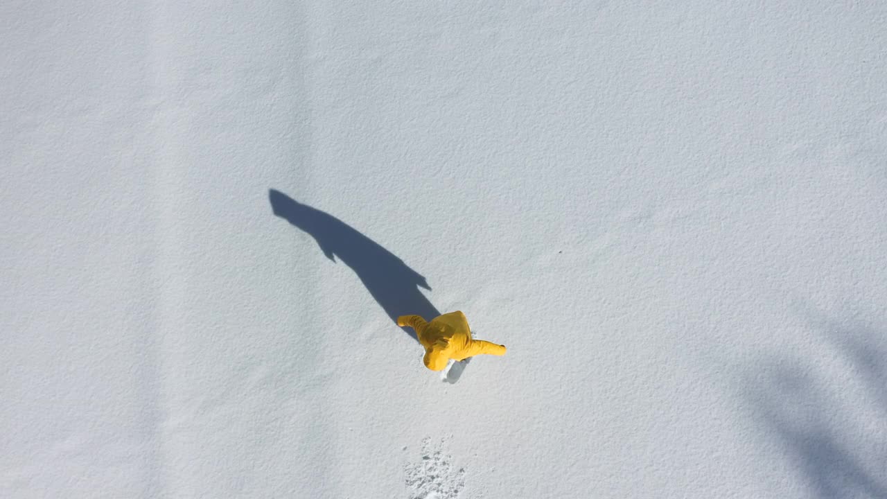一个穿着黄色夹克的男人躺在厚厚的雪地上做天使的鸟瞰图视频下载