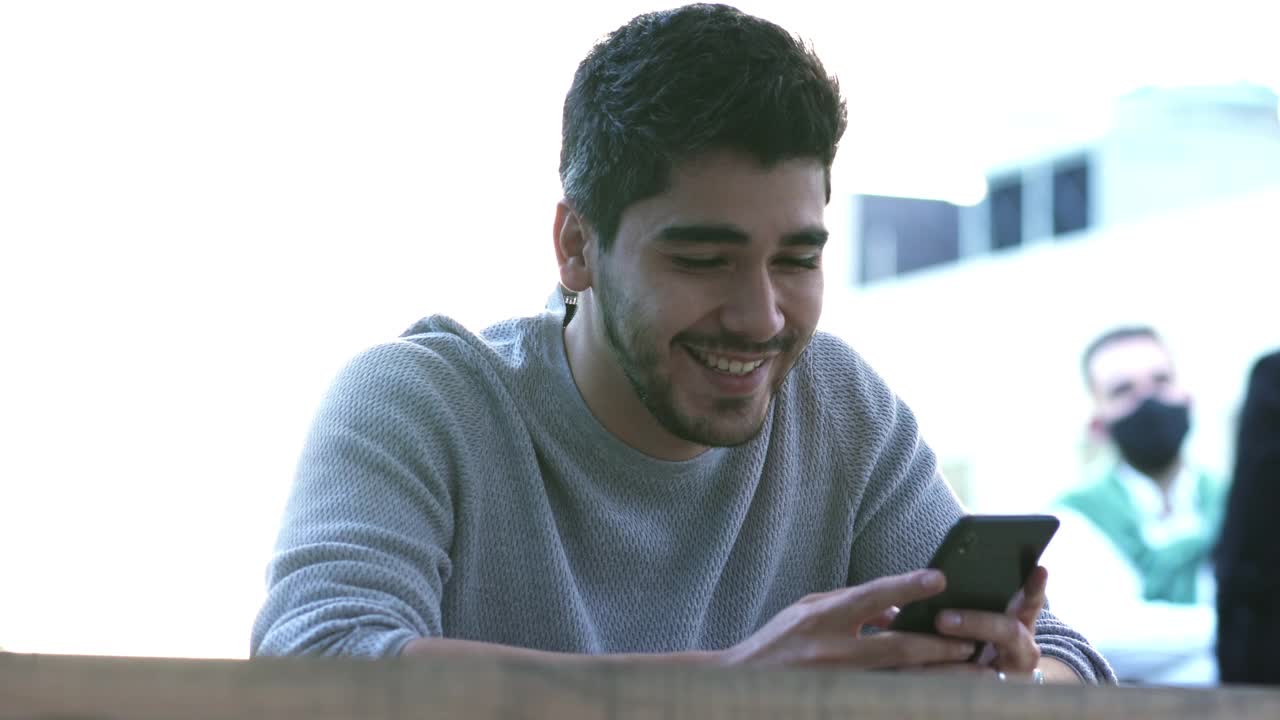 20岁的拉丁裔男子坐在购物中心通过手机发送语音信息视频素材