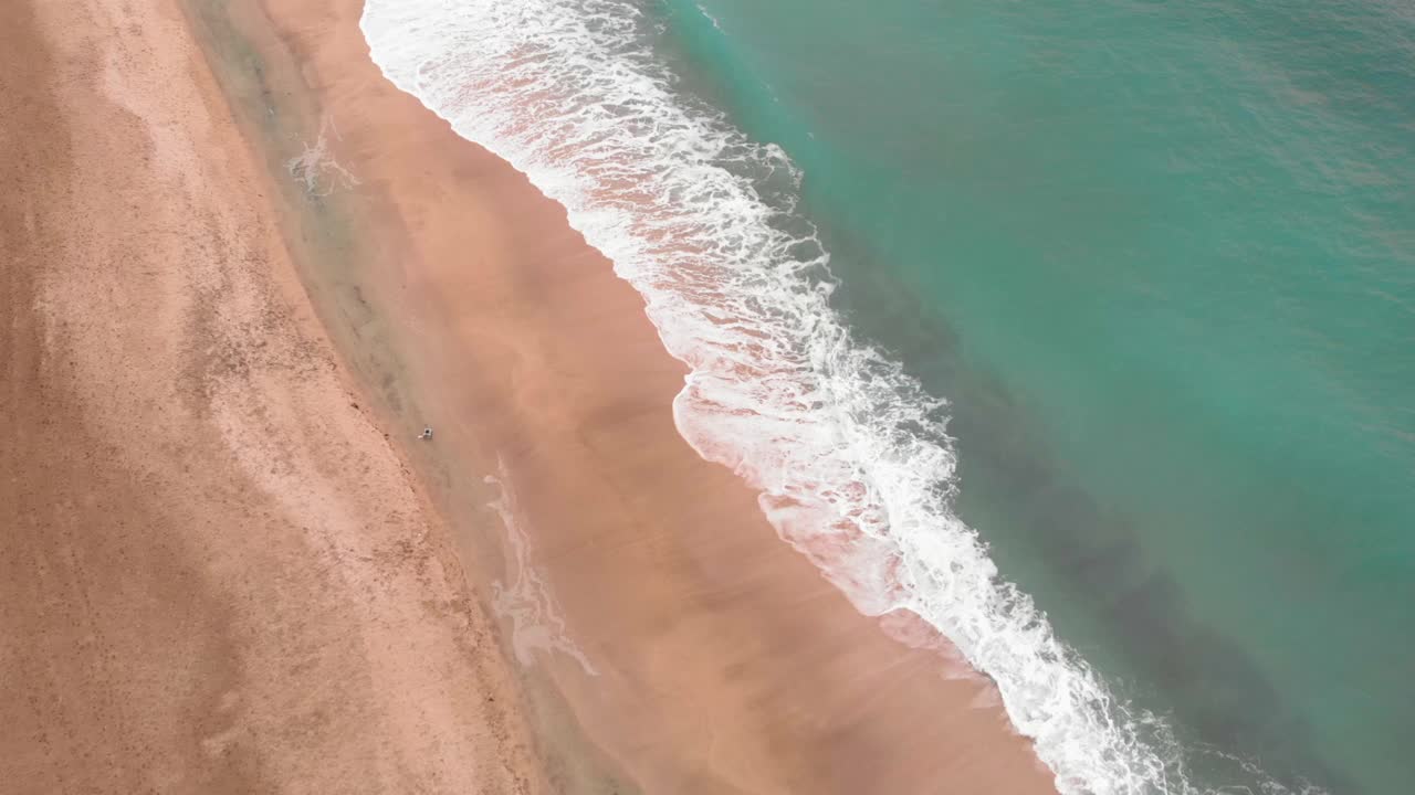 碧绿的海浪拍打着沙质海岸线。金色的海滩，深蓝色的海水和白色的泡沫，无人机拍摄视频素材