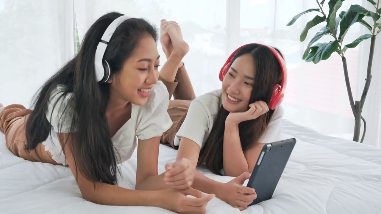 快乐的亚洲女性喜欢躺在平板电脑上戴着耳机听音乐视频素材