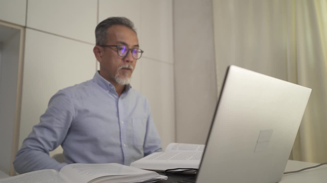 亚洲华人资深男教授家教老师给他的成年学生使用笔记本电脑在家里工作视频素材