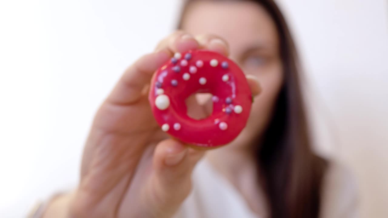在一个特写镜头中，一名妇女用右手展示着一个圆形的甜甜圈，上面撒着红色的糖霜和彩色的糖屑。饮食概念视频素材