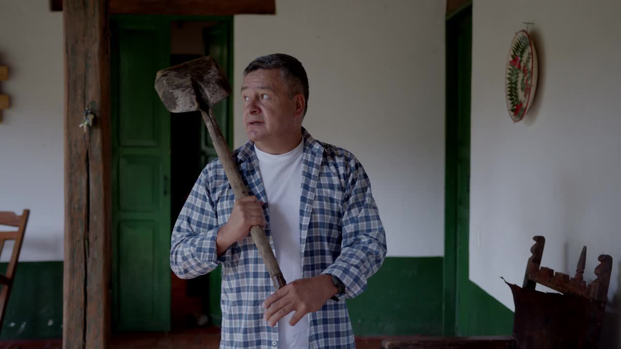 拉丁美洲的一名男性农民肩上扛着一把铁锹，从他家欣赏着窗外的景色视频素材