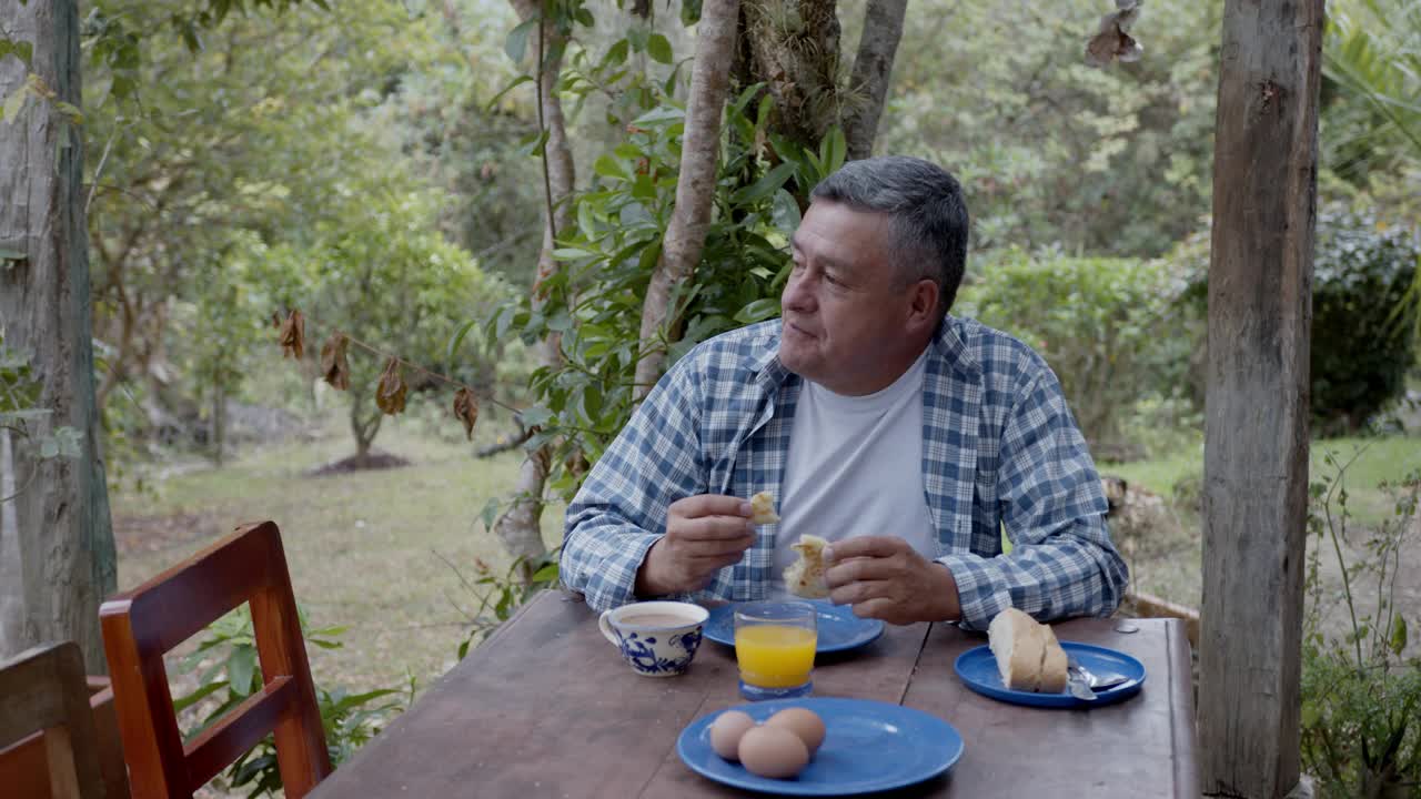 一个拉丁美洲的成年男子在郊外的家中一边吃早饭一边欣赏风景视频素材