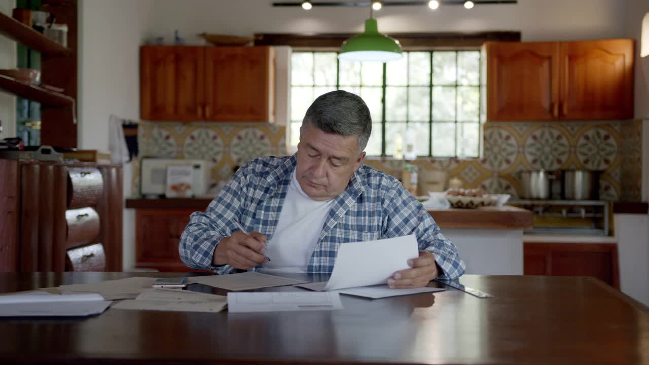 成年拉丁美洲男子在他乡下的家里用智能手机上的计算器组织他的财务视频素材