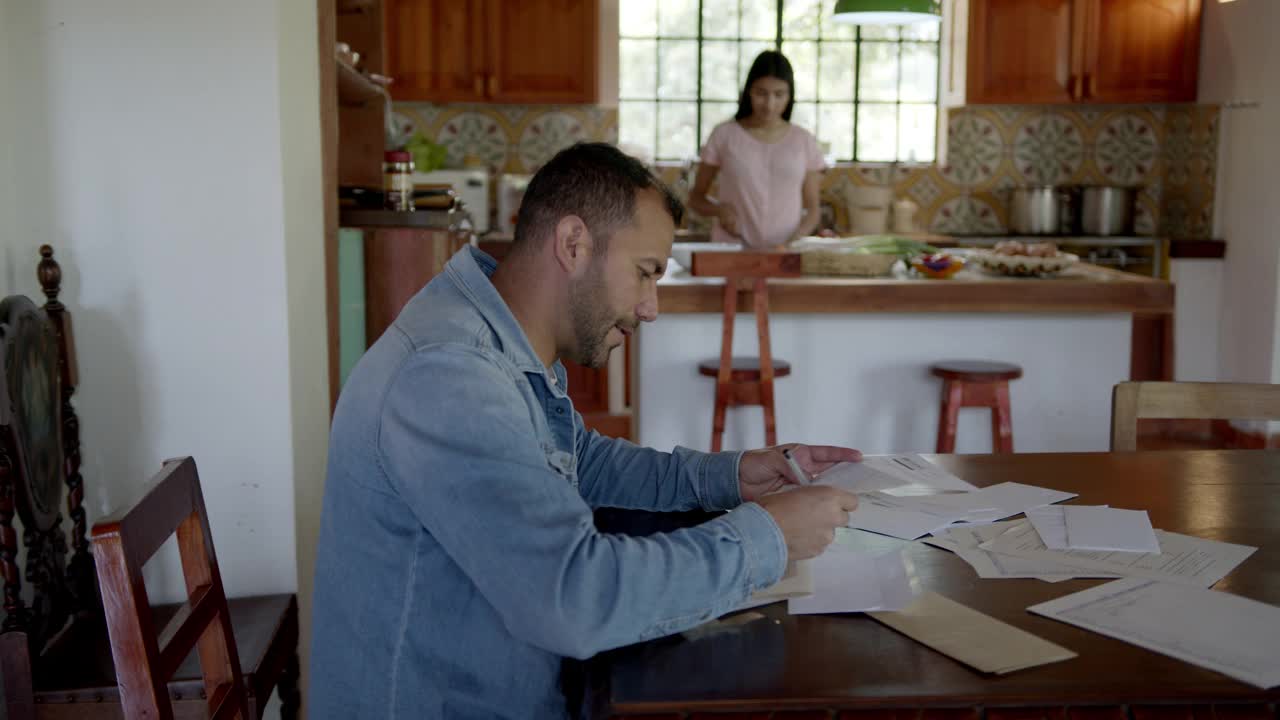 拉丁美洲男子工作与一些文件，而妻子在农村家庭做饭视频素材