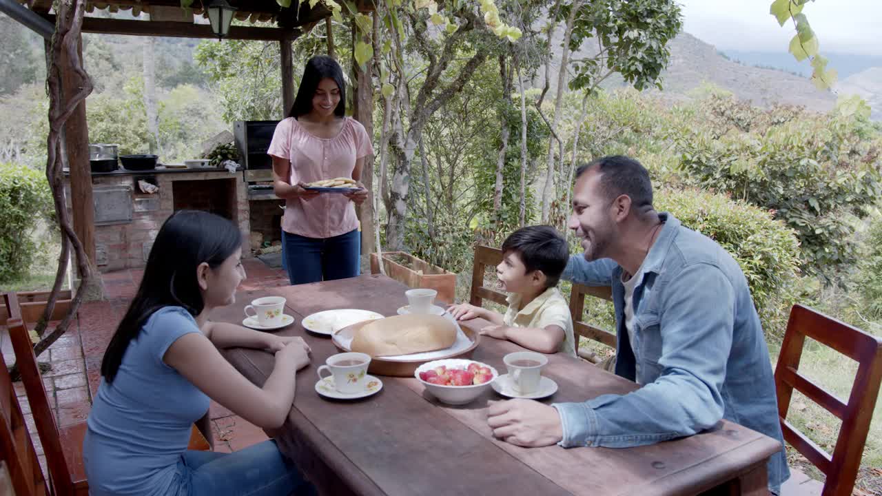 快乐的拉丁美洲妇女提供玉米饼，与她的家人在一个咖啡农场吃传统早餐视频素材