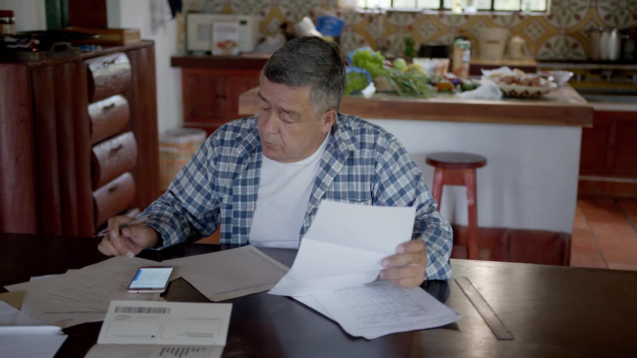 一个成熟的男人在他乡下的家里用智能手机看账单和整理他的财务视频素材