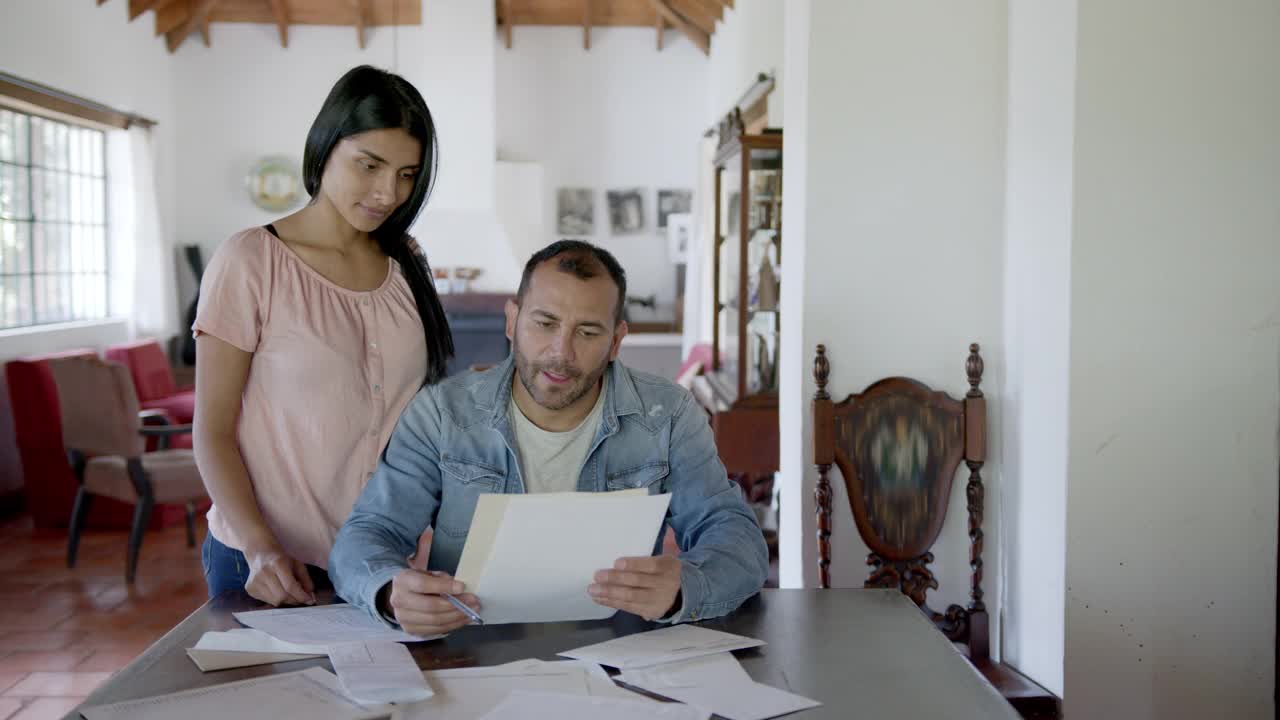 一对住在乡村房子里的拉美夫妇，一边看水电费账单一边组织他们的家庭财务视频素材