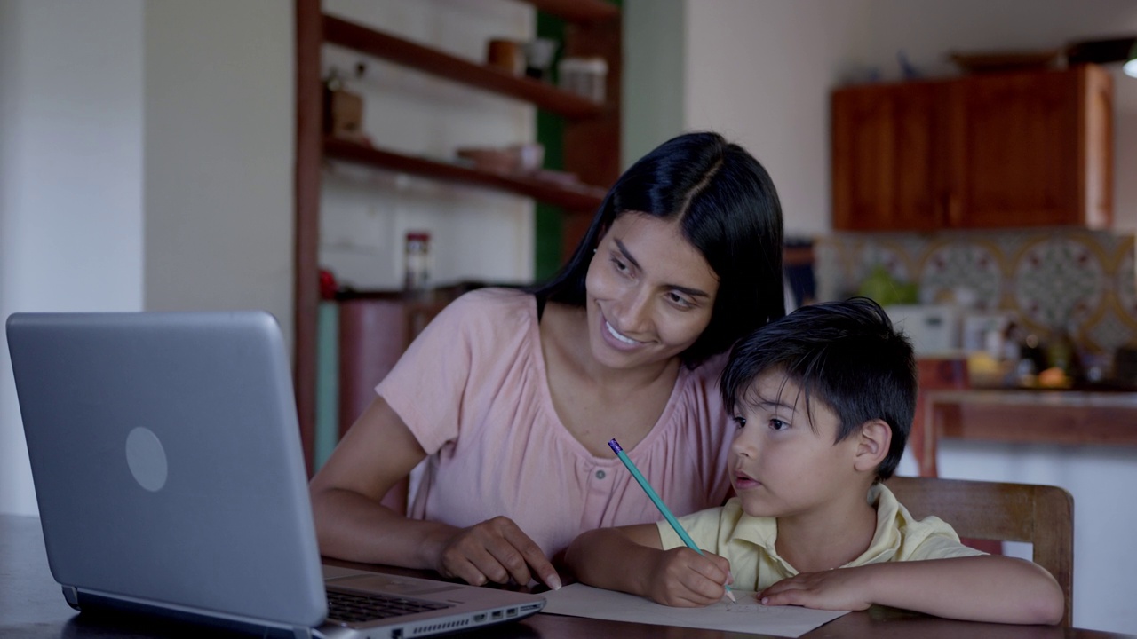 快乐的拉丁美洲母亲在家里用笔记本电脑在线学习时监督她的儿子视频下载
