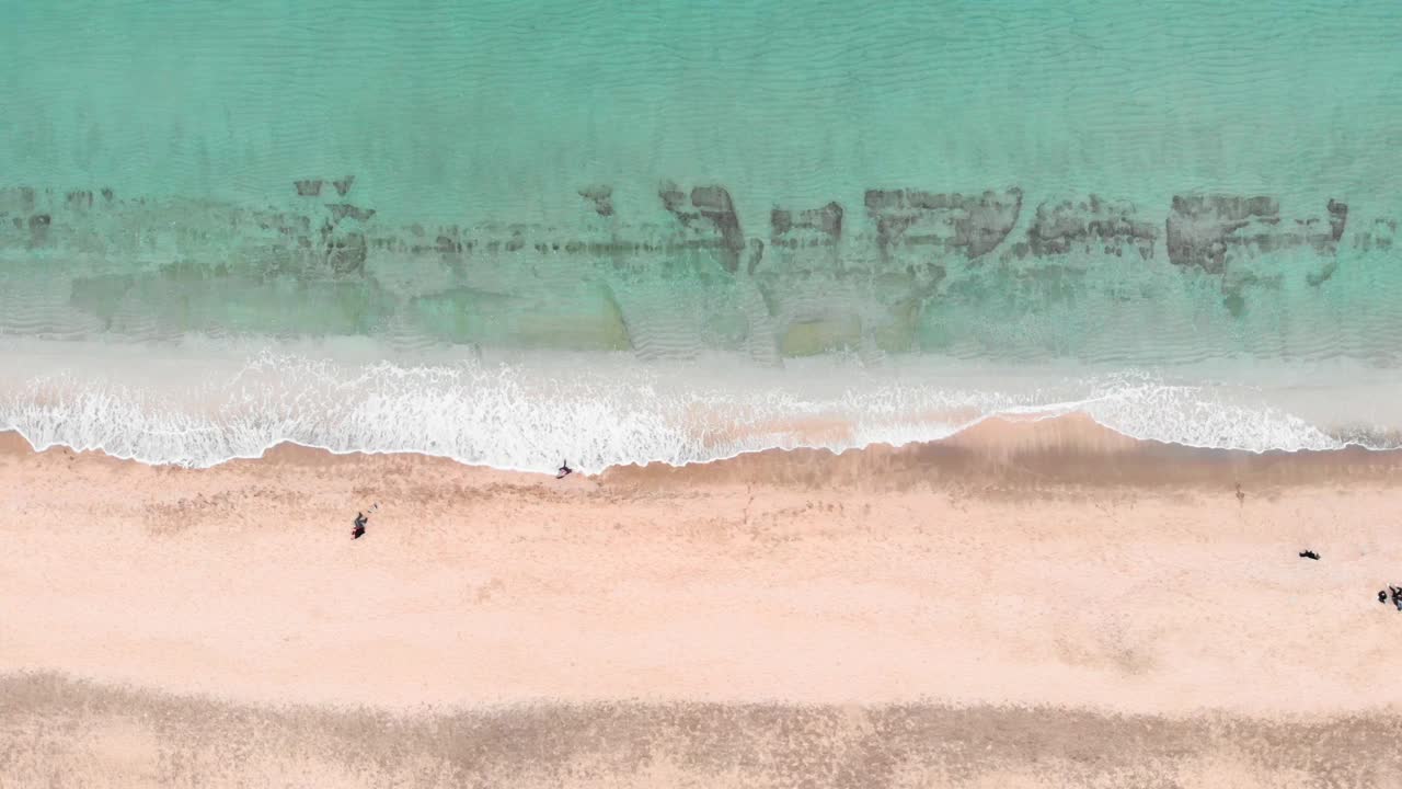 清澈的绿松石海水和金色沙滩，鸟瞰图。海浪拍打着，产生白色的泡沫，撞击着海滩。神奇的景观视频素材