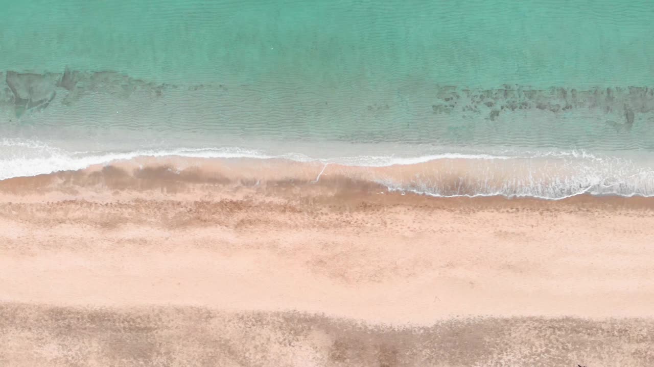 空中俯瞰惊人的蓝色清澈的海浪打破沙滩。金色的海滩，绿松石般的海水。海浪拍打着沙滩。令人难以置信的海上风景视频素材
