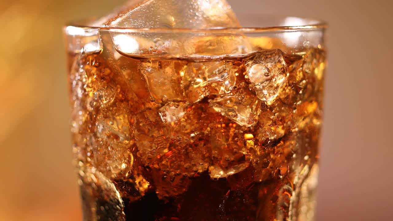 一杯有冰块的可乐。可乐饮料与冰和泡沫在玻璃近距离。在模糊的背景上旋转可乐杯。慢动作旋转4K视频片段视频素材