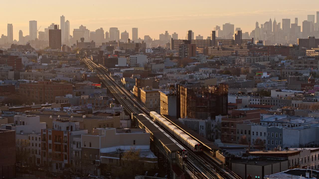 从住宅区远眺布鲁克林市中心和曼哈顿。傍晚，一列火车沿着默特尔大道沿着高架地铁开往布鲁克林市中心。无人机视频与前摇摄像机运动。视频素材