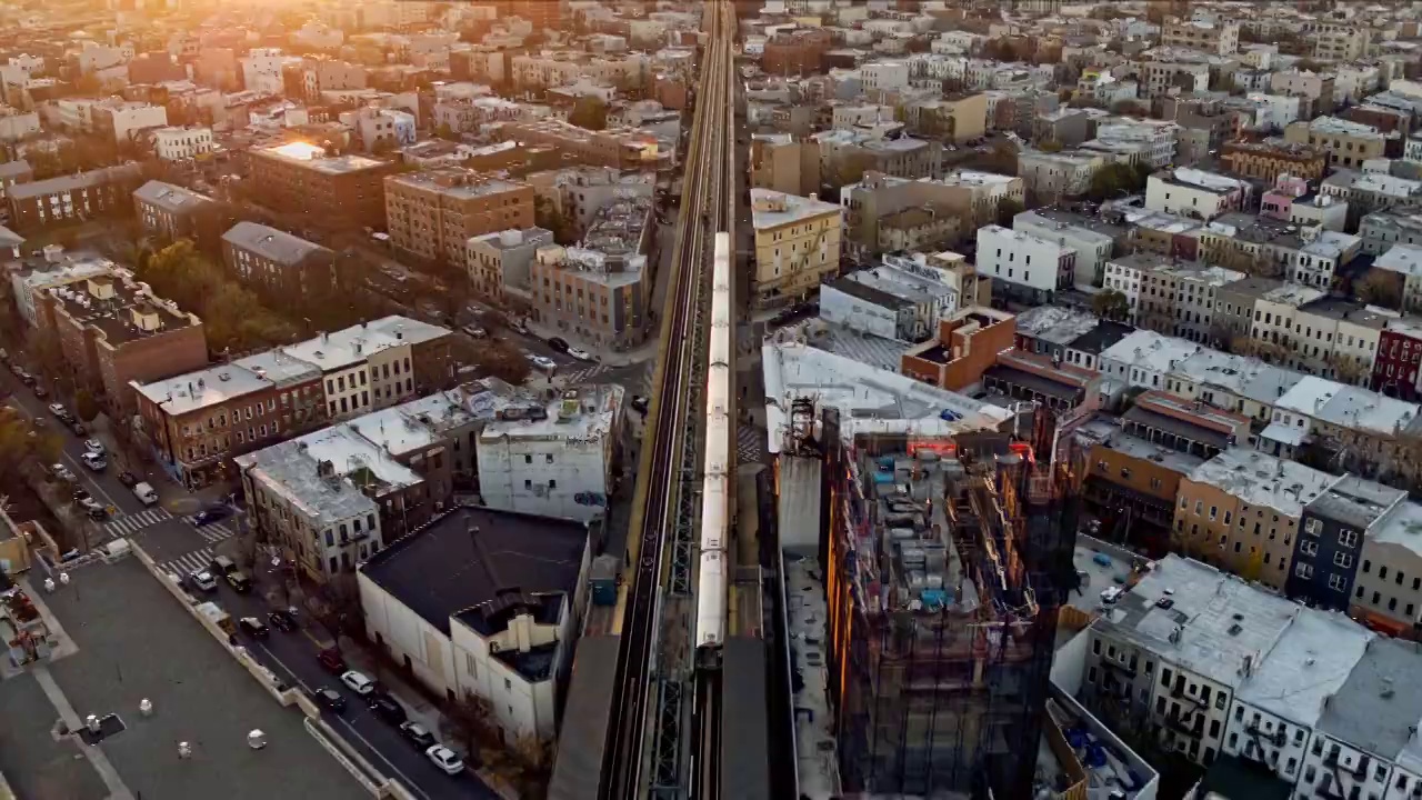日落时分，一列火车正穿过纽约布鲁克林的住宅区。无人机视频与向前和倾斜加速摄像机运动。视频素材