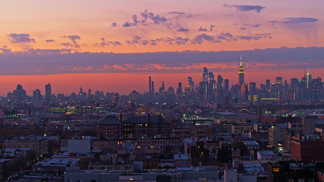 曼哈顿天际线在布鲁克林布什威克住宅区的夜晚被照亮的远景，在日落中。无人机视频与平移摄像机运动。视频素材