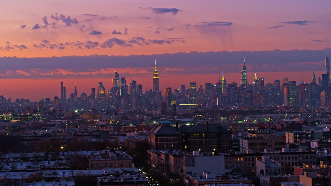 曼哈顿天际线在布鲁克林布什威克住宅区的夜晚被照亮的远景，在日落中。无人机视频与平移轨道摄像机运动。视频素材
