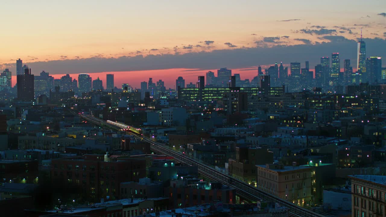 曼哈顿下城和布鲁克林下城的空中遥视，在夜晚照亮，在布什维克住宅区，在日落。一列火车正从地铁线高架上驶过。用静态摄像机拍摄无人机视频。视频下载