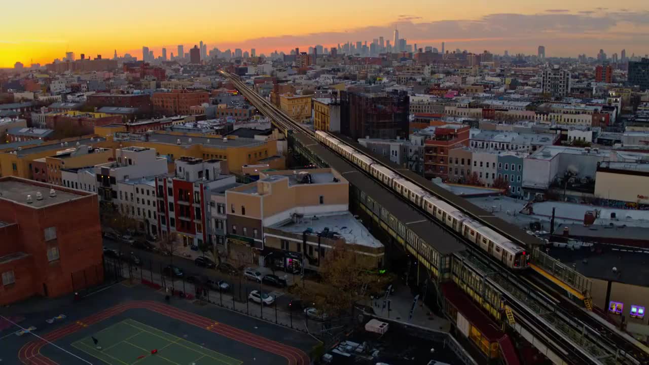 一列火车从车站出发，从布什威克俯瞰住宅区，俯瞰布鲁克林市中心和曼哈顿天际线的高空广角全景。无人机视频与向前摄像机运动。视频素材