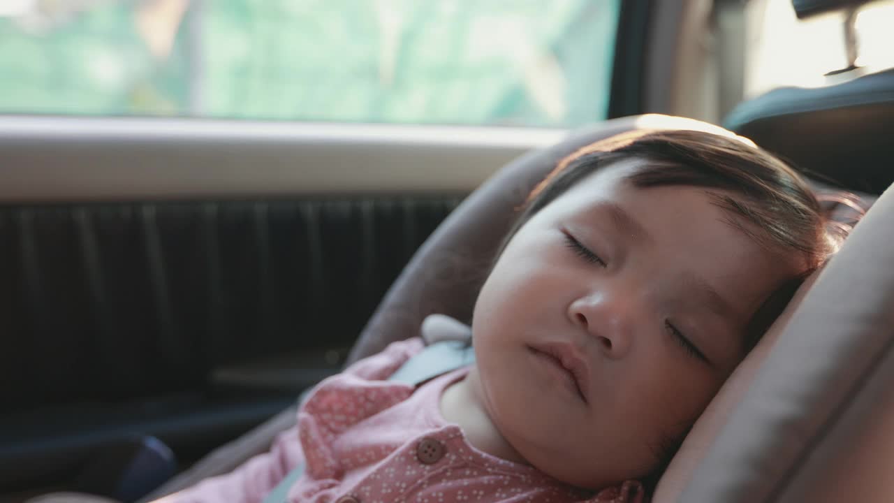近距离拍摄可爱的亚洲蹒跚学步的女孩坐在汽车座椅和睡觉，而旅行与家人在慢镜头。视频素材