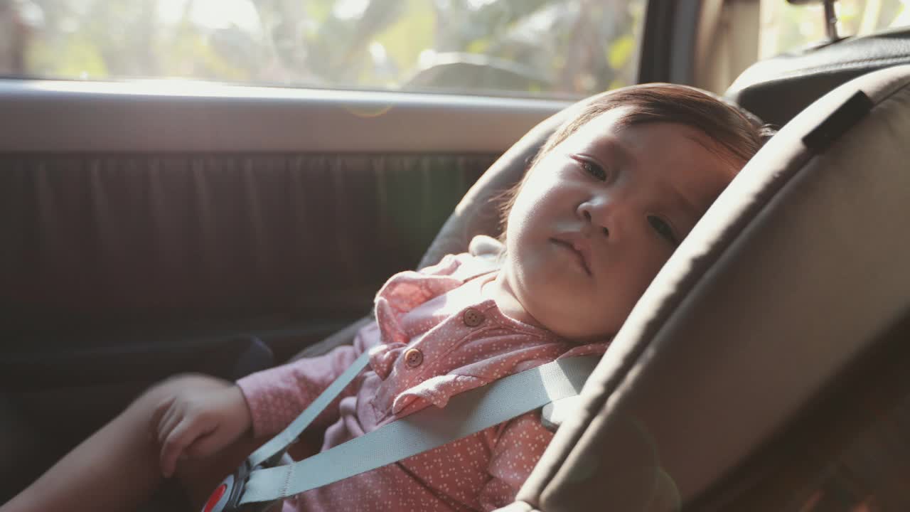 可爱的亚洲蹒跚学步的女孩坐在汽车座椅和感觉困倦而与家人旅行的慢动作。视频素材
