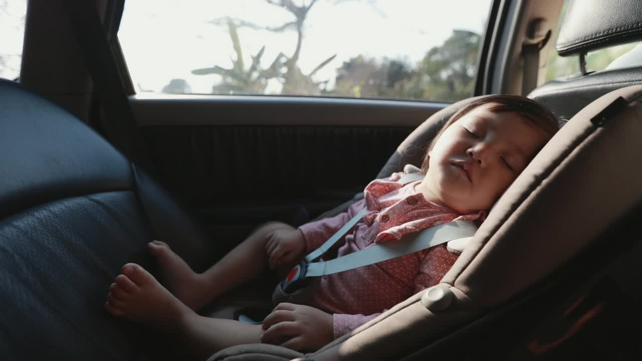 可爱的亚洲蹒跚学步的小女孩坐在汽车座椅上，和家人一起旅行时睡觉。视频素材
