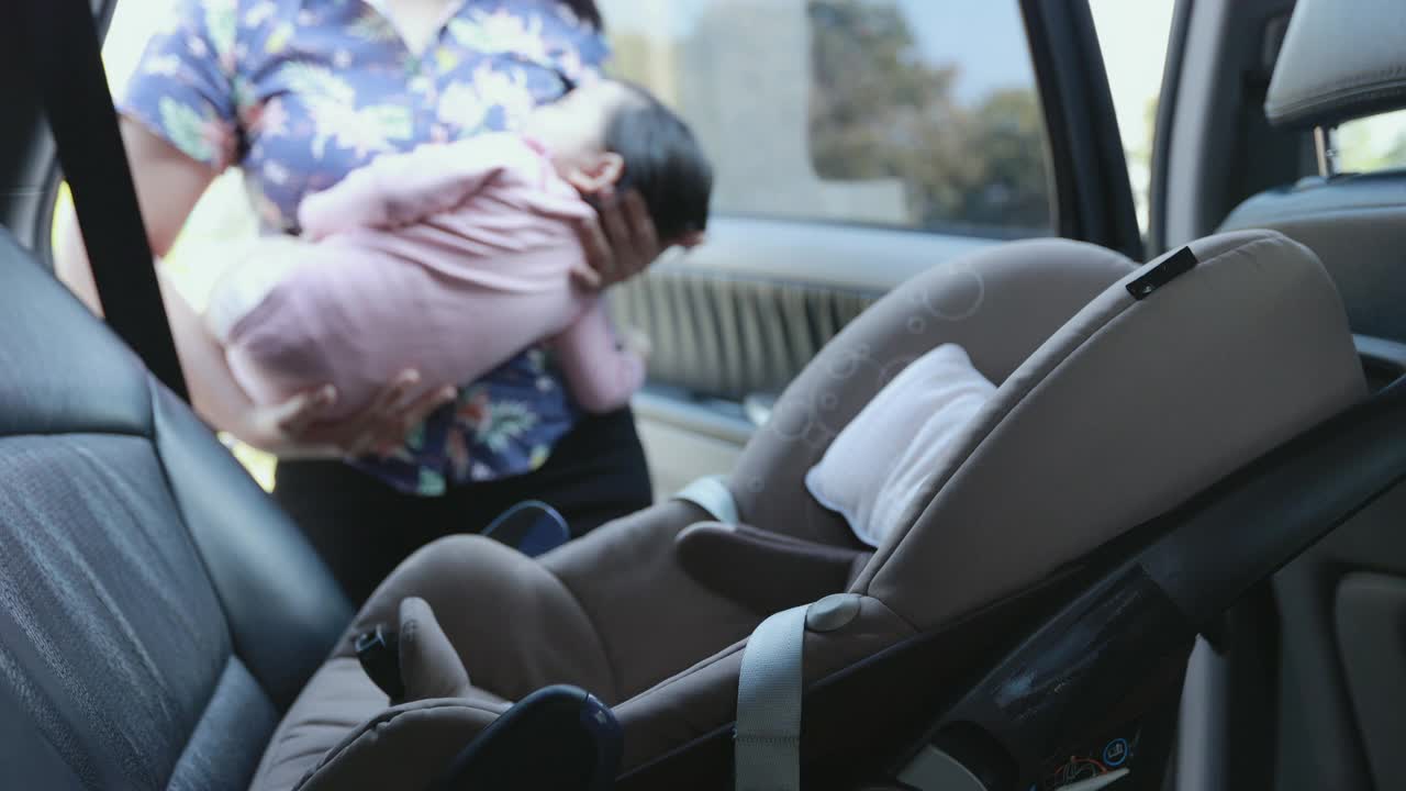 亚洲母亲抱着她的女儿，当她在车里睡觉，并把汽车安全带给她的女儿。可爱的亚洲蹒跚学步的女孩哭和困倦坐在汽车座位上。视频下载