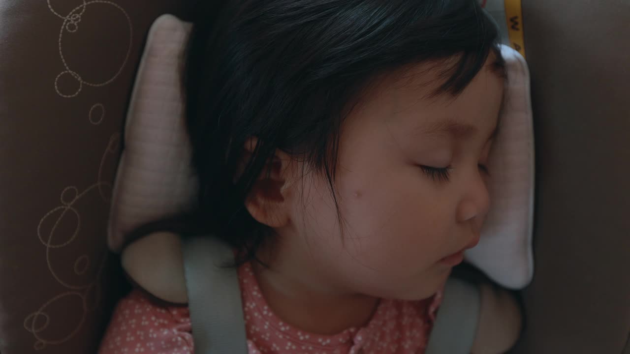 近距离观察可爱的亚洲蹒跚学步的女孩坐在汽车座椅和睡觉，而与家人旅行。视频素材