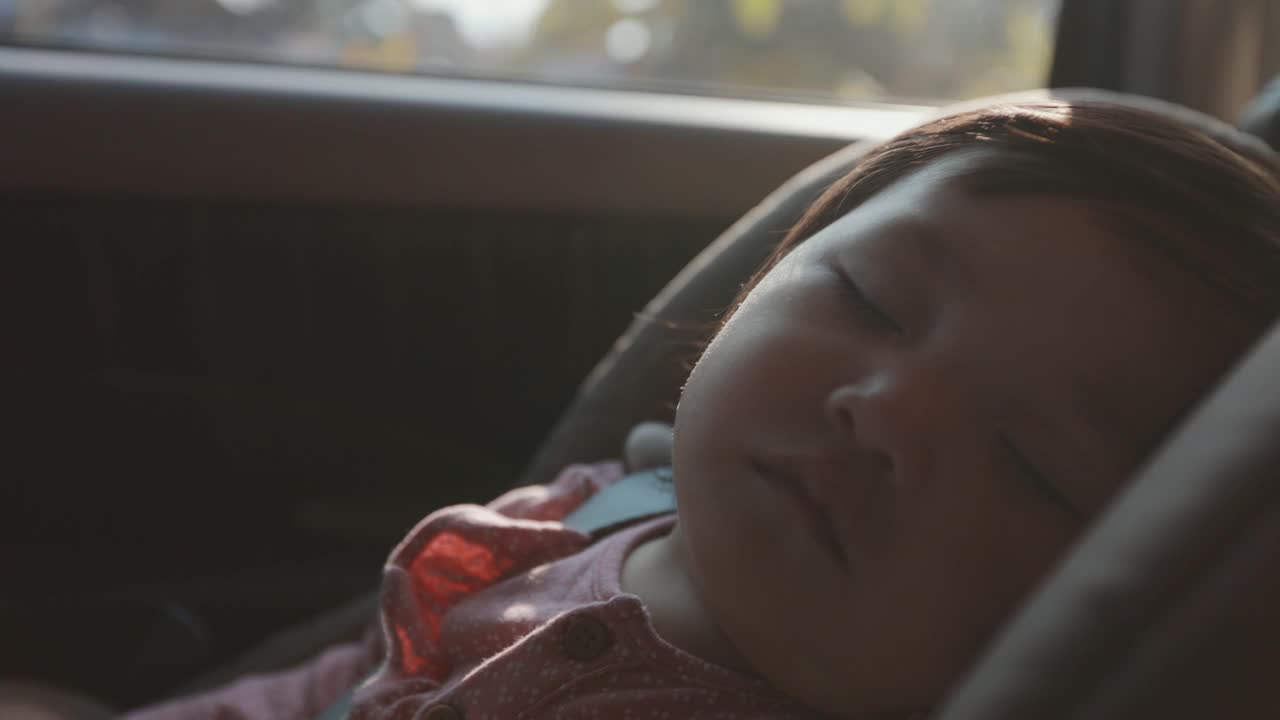 近距离拍摄可爱的亚洲蹒跚学步的女孩坐在汽车座椅和睡觉，而旅行与家人在慢镜头。视频素材