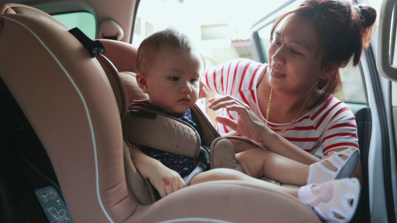 亚洲母亲把她的女儿放在汽车座椅和系安全带的女儿公路旅行。视频素材