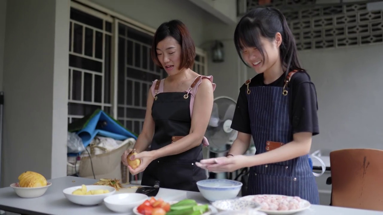亚裔华人母亲和女儿在后院厨房准备食物。女儿在向母亲学习视频下载