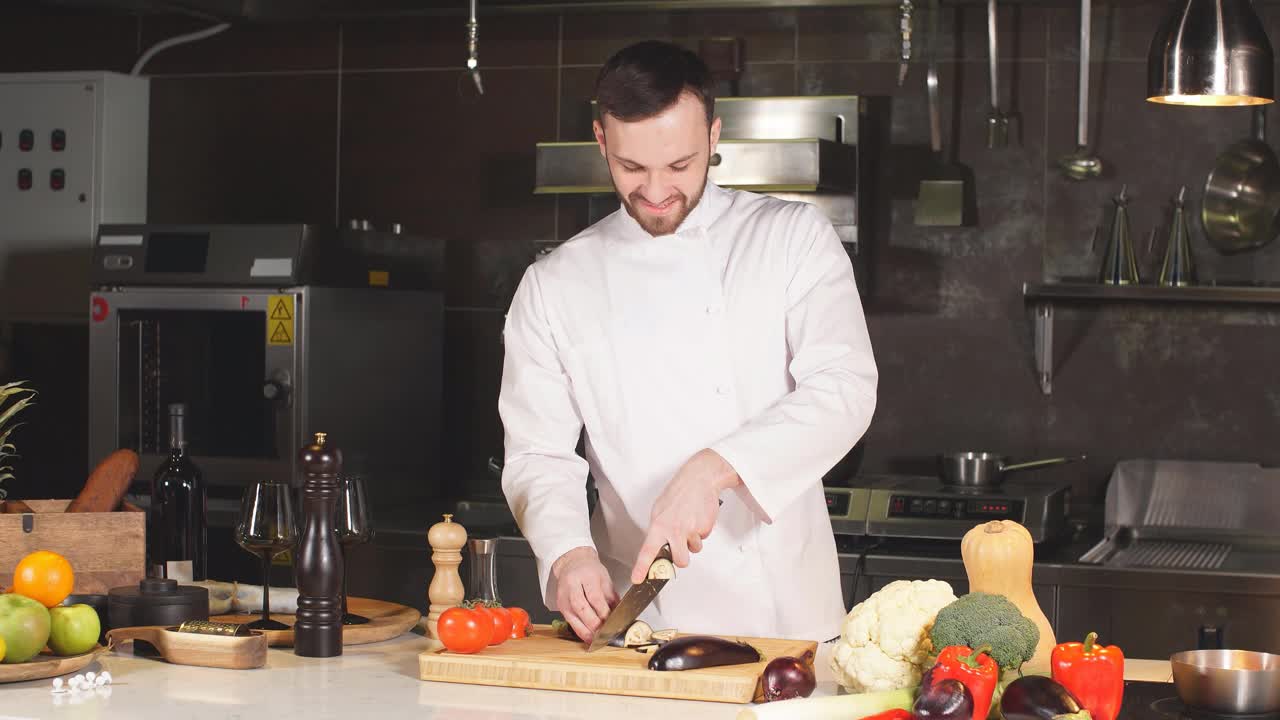 在现代餐厅的厨房里，年轻的厨师在一块木板上切茄子视频下载