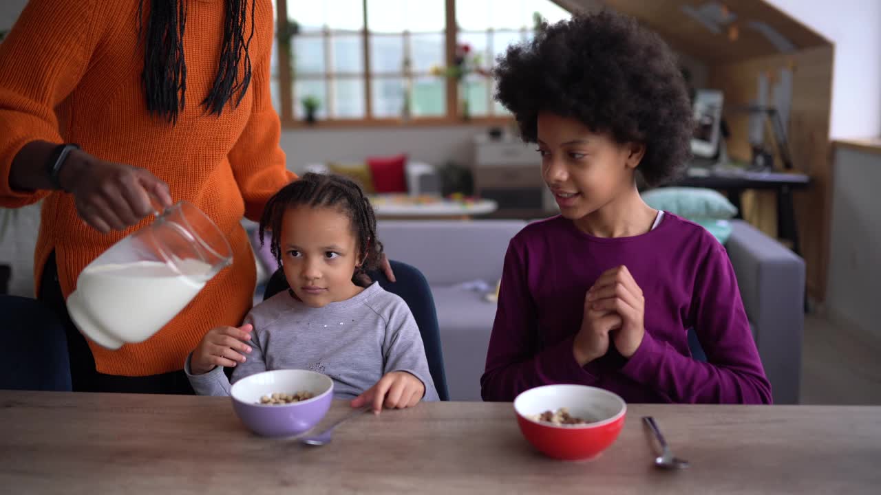 两个可爱的非洲女孩吃麦片早餐，而他们的母亲正在客厅放松视频下载
