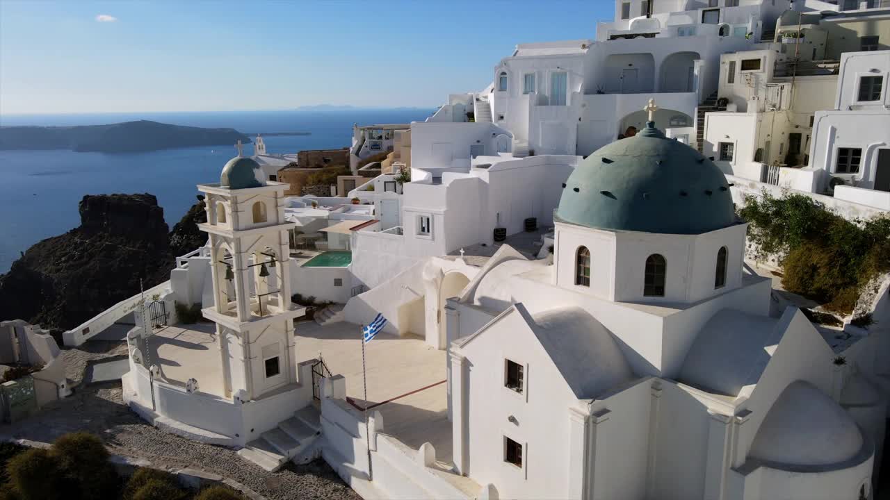 航拍城市里著名的阿纳斯塔西东正教教堂，在阳光明媚的日子里，无人机在白色建筑上向前飞行——希腊圣托里尼视频素材