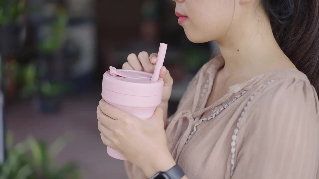 一个陌生的亚洲女人用硅胶旅行杯喝水视频素材