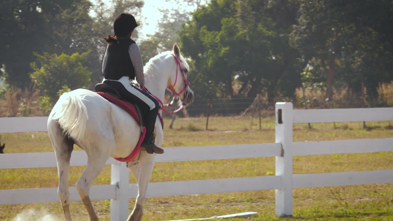 年轻的亚洲女孩喜欢在农场骑马，女孩在农场骑马训练，她骑着一匹白色的阿拉伯马在泰国视频下载