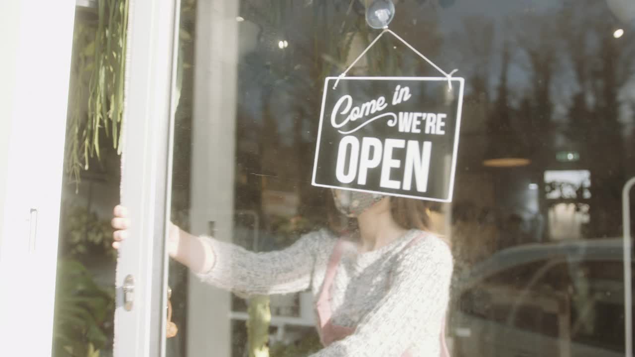 在冠状病毒大流行期间，小企业企业家戴着口罩为顾客打开商店大门。视频素材