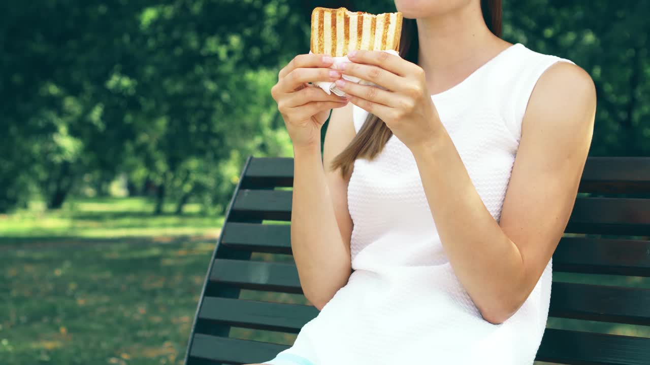 饥饿的女人在公园吃三明治。游客在公园享用午餐，享受夏日的阳光视频素材
