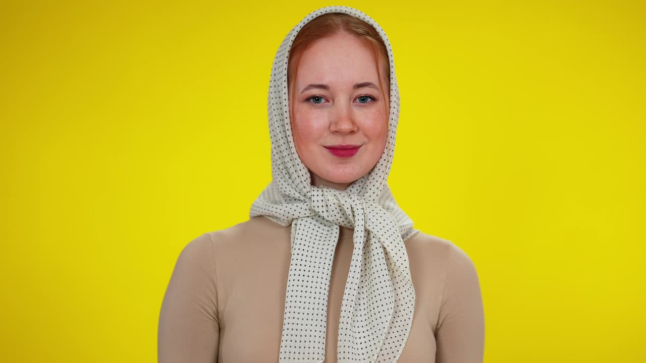 年轻苗条的红发女人在黄色背景摆姿势的头巾肖像。微笑美丽的白人女士看着镜头微笑。害羞和生活方式视频下载